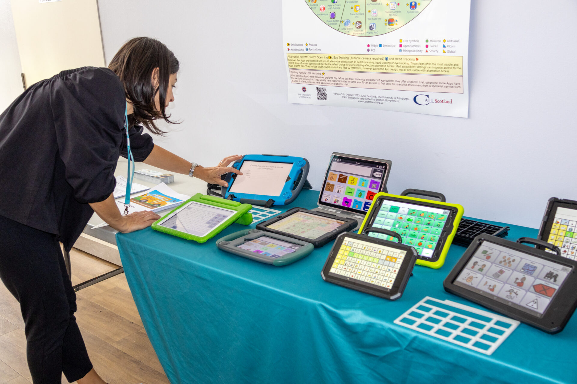 A young woman looking at AAC communication devices laid out on a table.