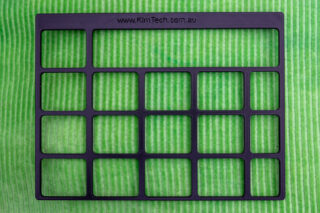 A black 3D printed keyguard for Grid for iPad VocoChat page set displayed on a green cushion.