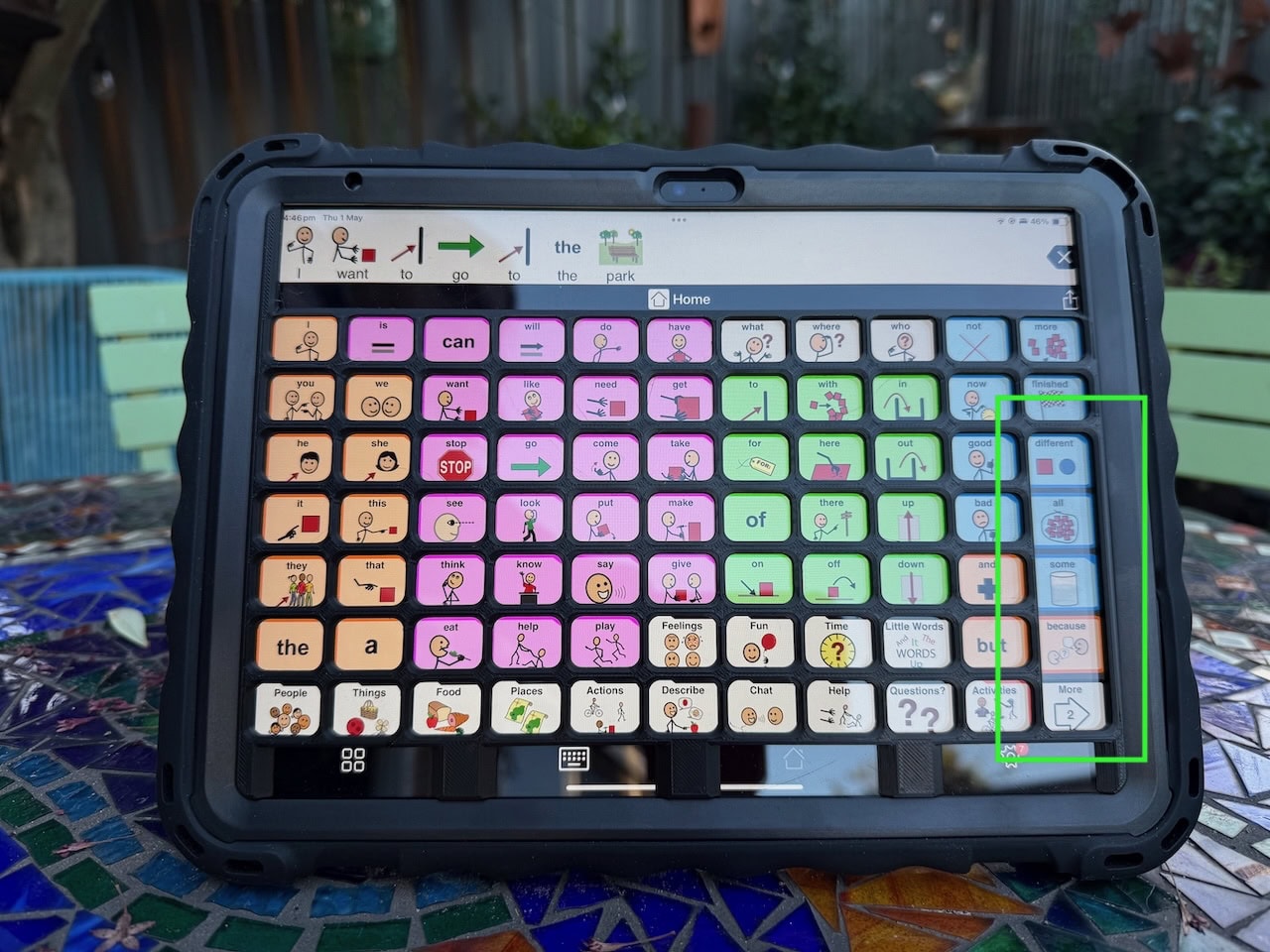 A black keyguard on an iPad with Proloquo2go page set displayed. The merged cells of the keyguard are highlighted.
